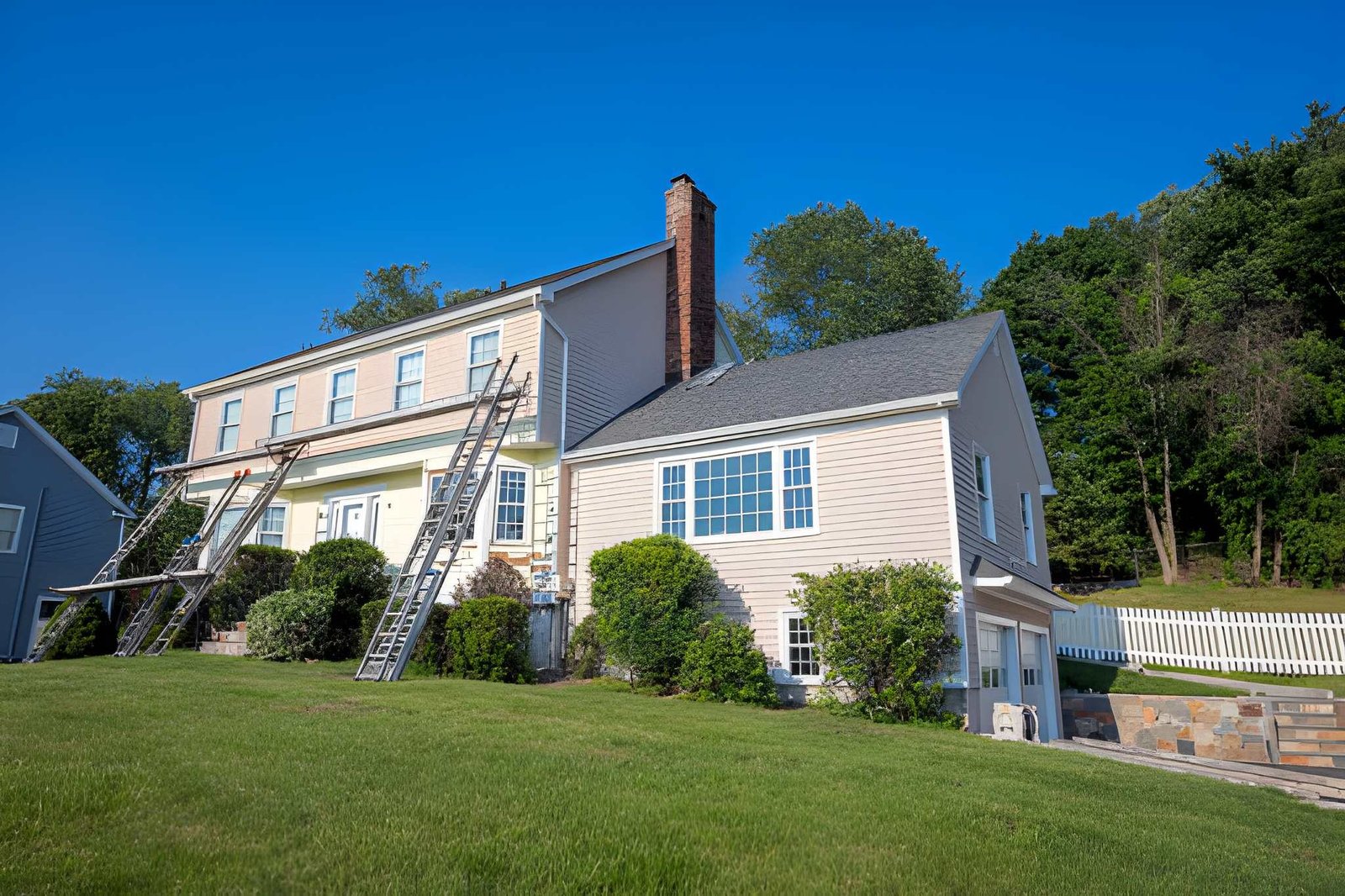 House exterior with ladders for siding services, beige siding, and chimney.