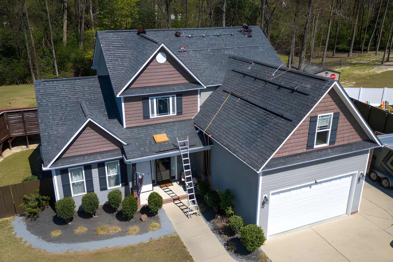 Roof installation in progress on a suburban house with grey shingles and brown accents.
