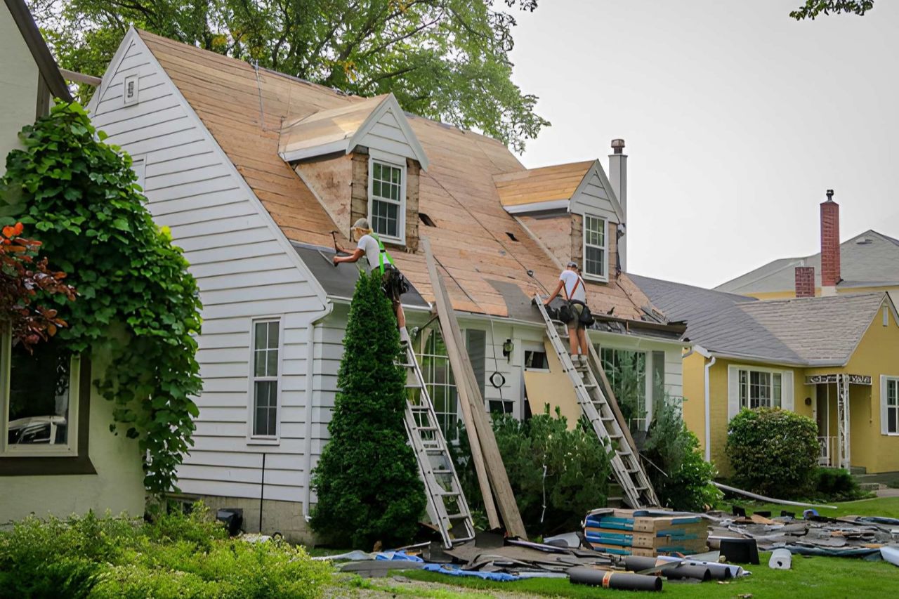 Roofers replacing shingles on a residential home, with siding visible.